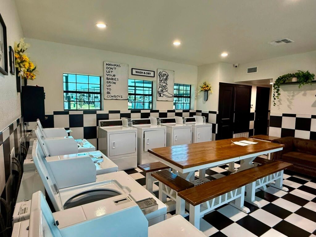 Guest laundry room with rows of washers and dryers, a wooden table and a black and white checkered floor