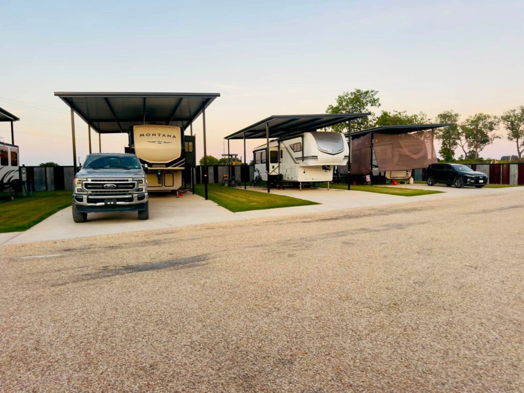 Fifth wheel RVs and a pickup truck parked under metal shade covers at Magnolia RV Resort