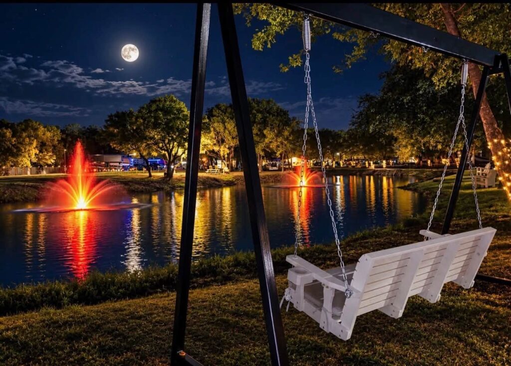 Lit pond fountain and porch swing at night at Magnolia RV Resort